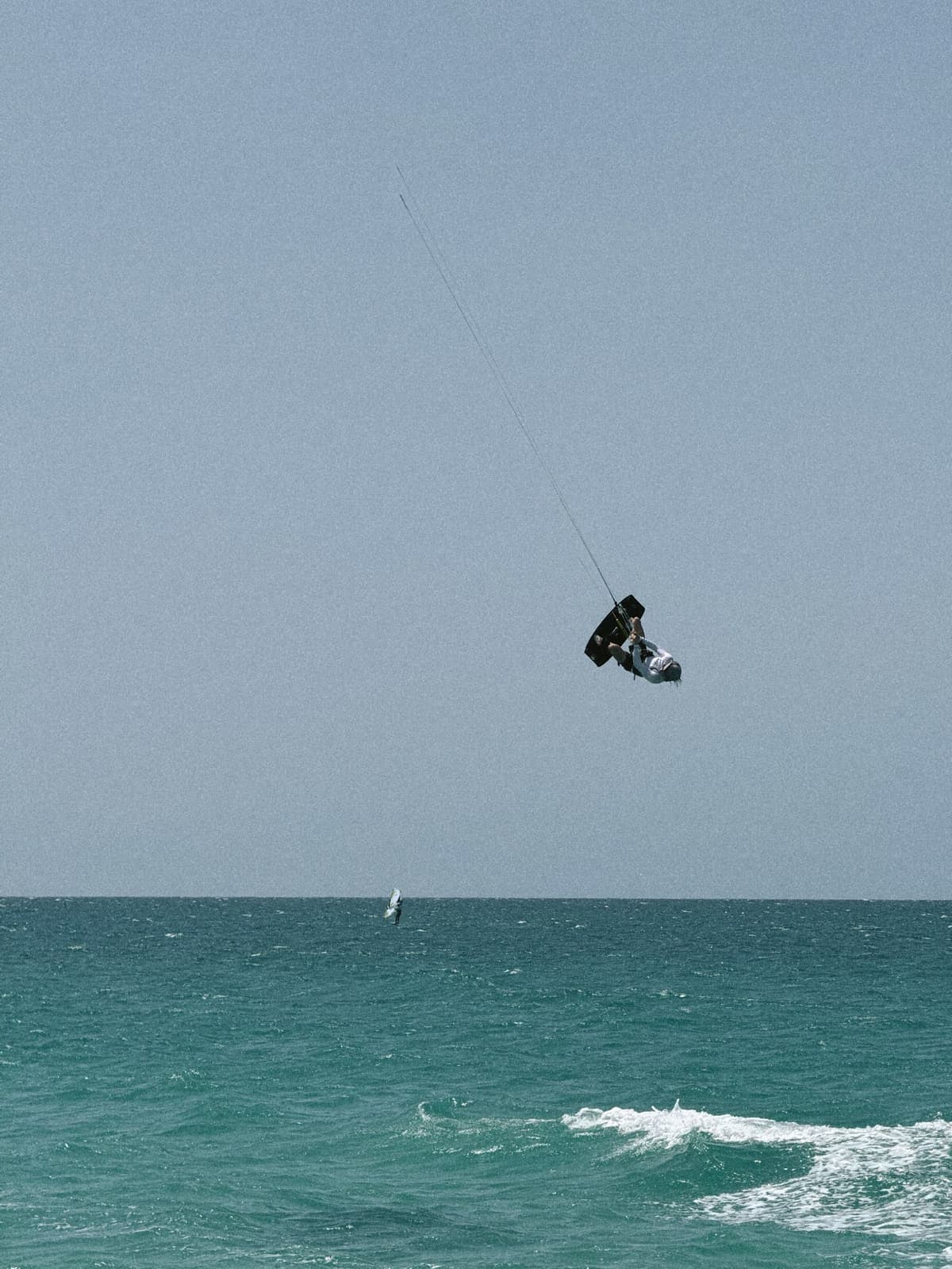 A kiter thrown upside down against a flat grey sky over teal water