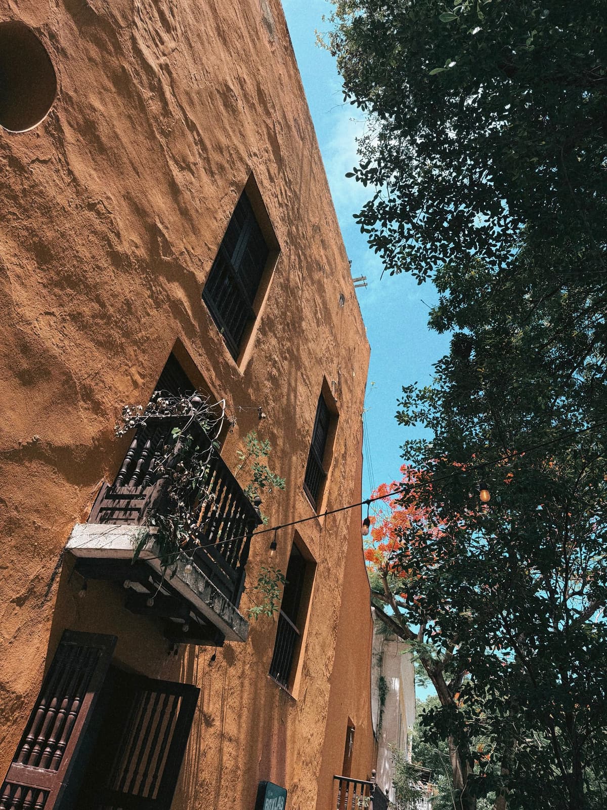 Looking up an ochre colonial wall, wrought-iron balcony against blue sky