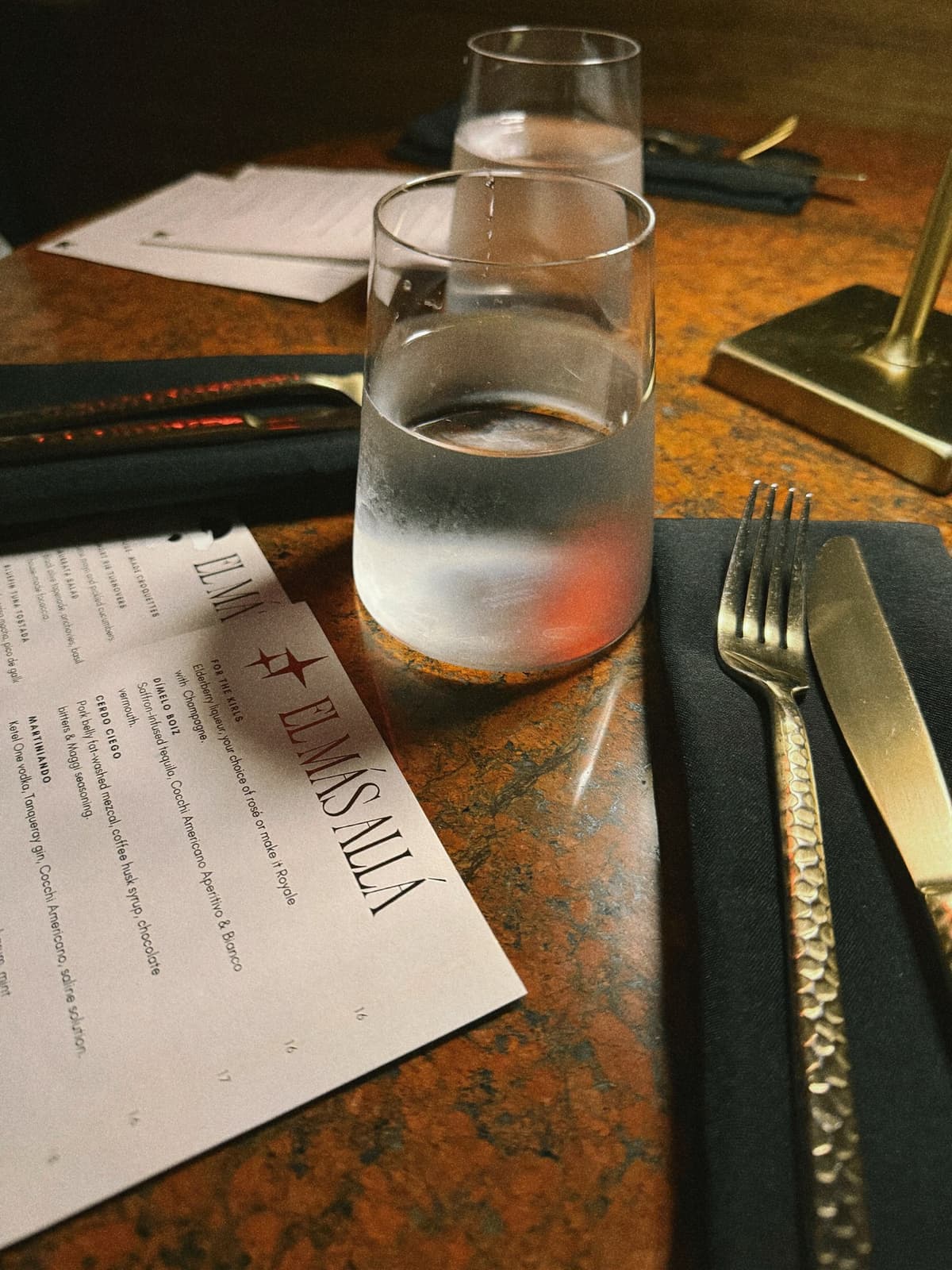 Water poured, menu open, brass and dark stone at the dinner table
