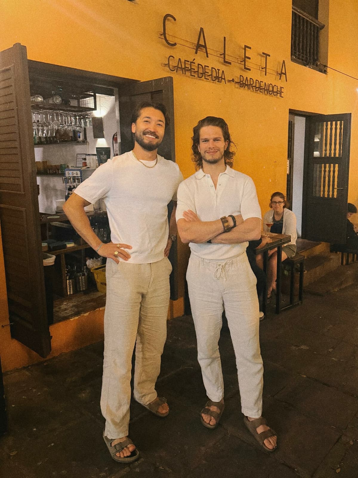 Two of us outside Caleta, linen and easy smiles against a yellow wall