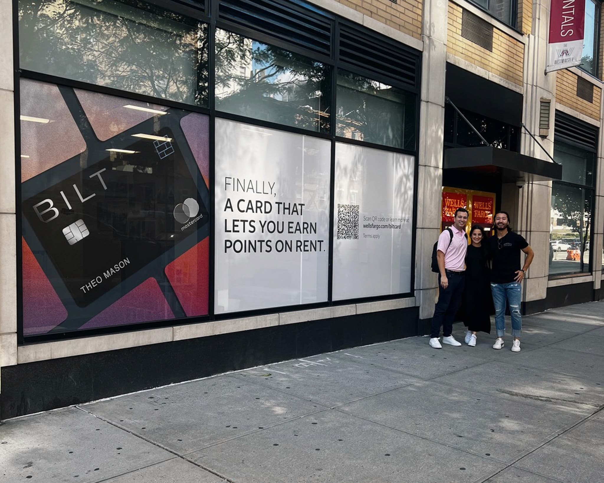 Wells Fargo branch storefront with full-window Bilt vinyl reading 'Finally, A Card That Lets You Earn Points on Rent'